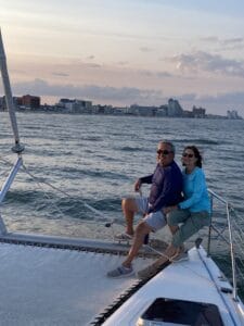 Couple relaxing on catamaran trampoline during Ocean Sailing Advanced trip with Ocean City skyline at sunset