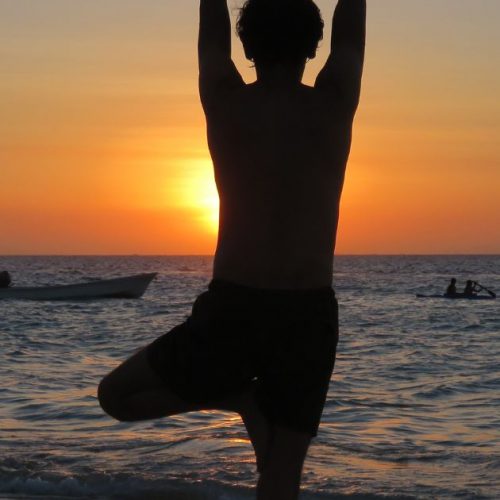 Person practicing tree pose yoga at sunset on Ocean City beach with ocean view