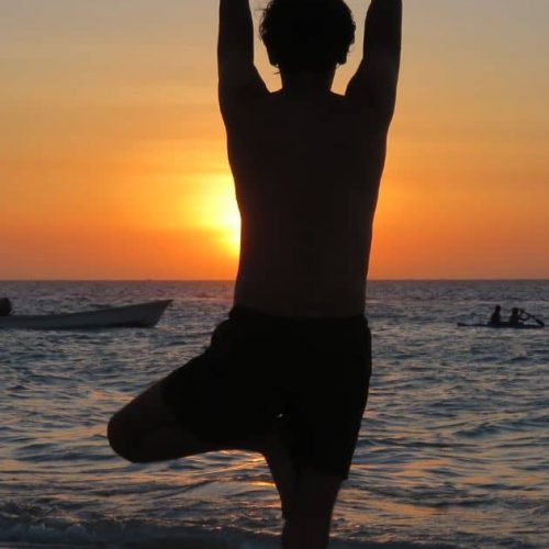 Person practicing tree pose yoga at sunset on Ocean City beach with ocean view