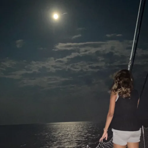 Full moon rising over Atlantic Ocean during moonlight sailing cruise aboard Alyosha catamaran off Ocean City Maryland coast with guest facing the moon