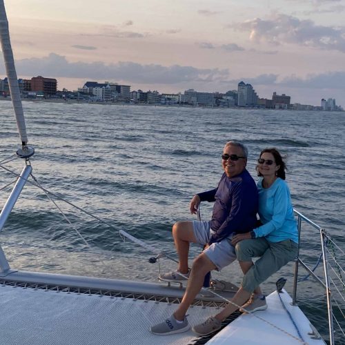 Couple relaxing on catamaran trampoline during Ocean Sailing Advanced trip with Ocean City skyline at sunset